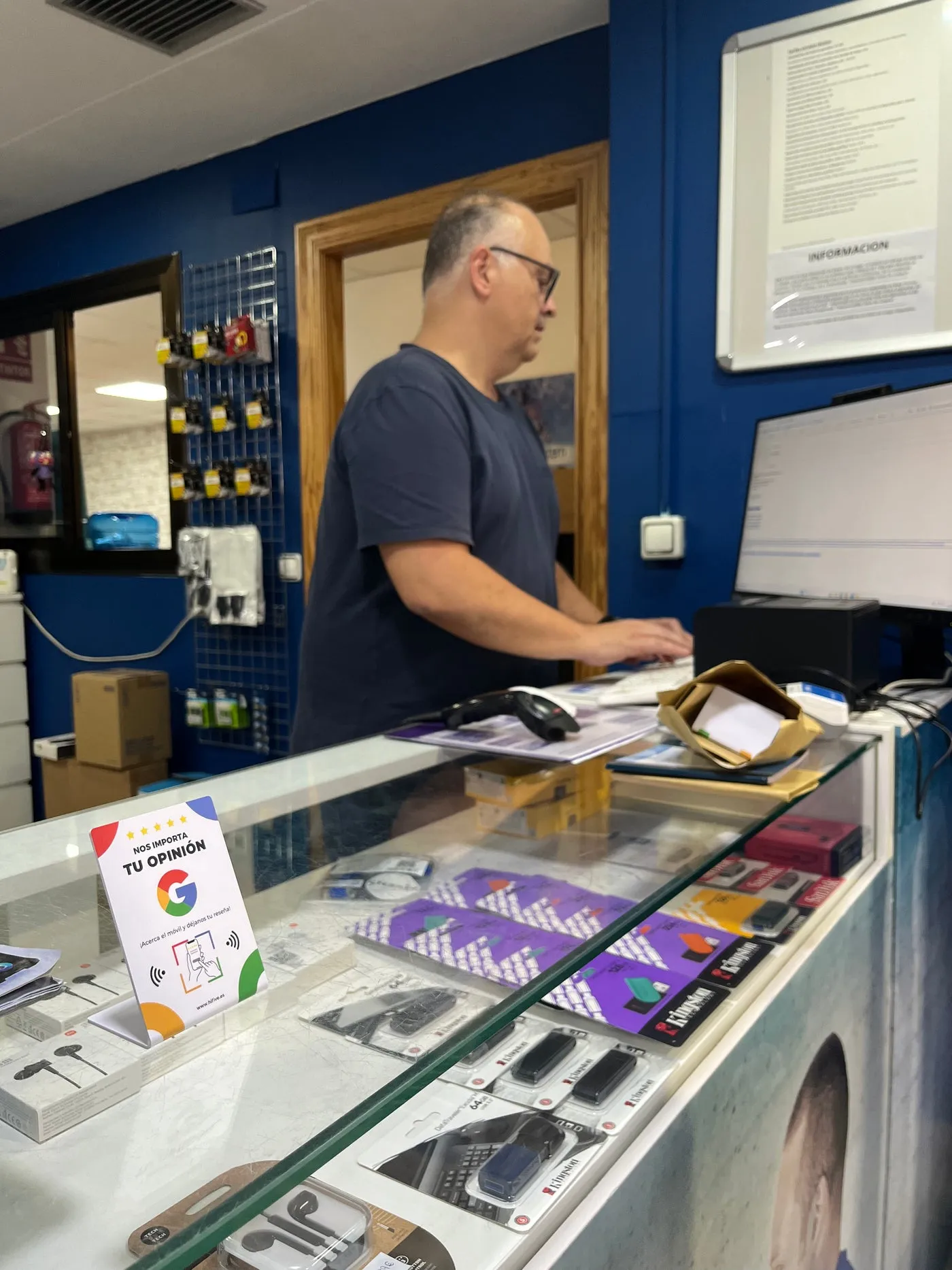 Expositor de Hifive sobre el mostrador de cristal de una tienda de telefonía, con el dueño detrás